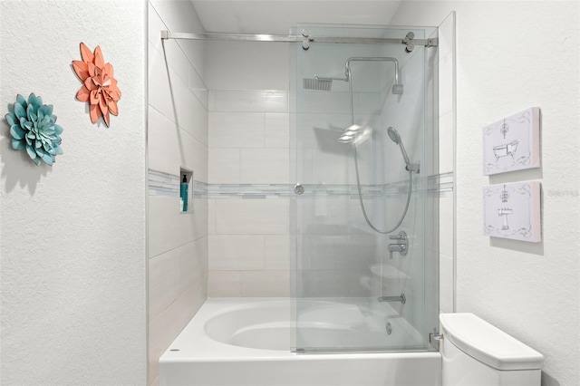 bathroom featuring toilet and shower / bath combination with glass door