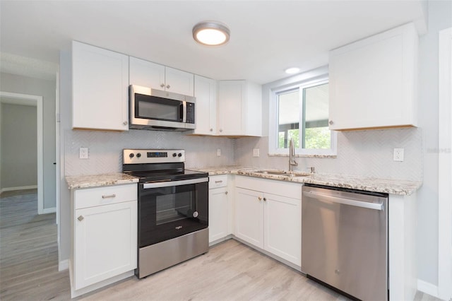 kitchen featuring white cabinets, light wood-type flooring, light stone counters, stainless steel appliances, and sink