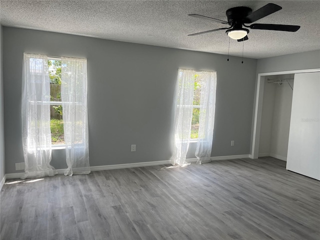 unfurnished bedroom with a textured ceiling, ceiling fan, hardwood / wood-style floors, and multiple windows