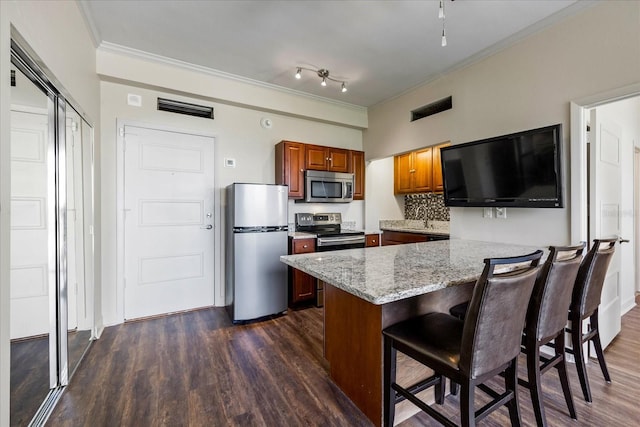 kitchen with stainless steel appliances, rail lighting, light stone counters, a breakfast bar area, and dark wood-type flooring