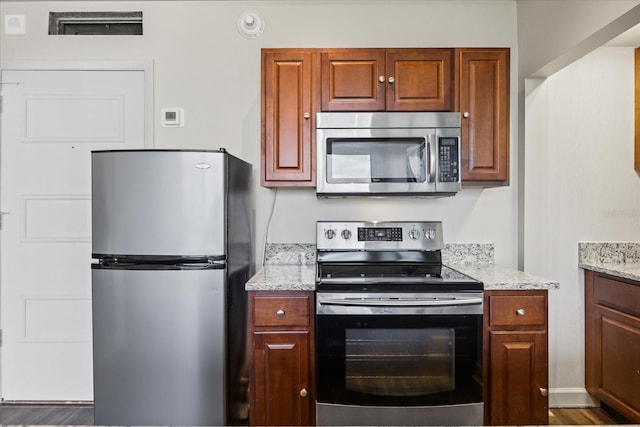 kitchen with appliances with stainless steel finishes, wood-type flooring, and light stone countertops