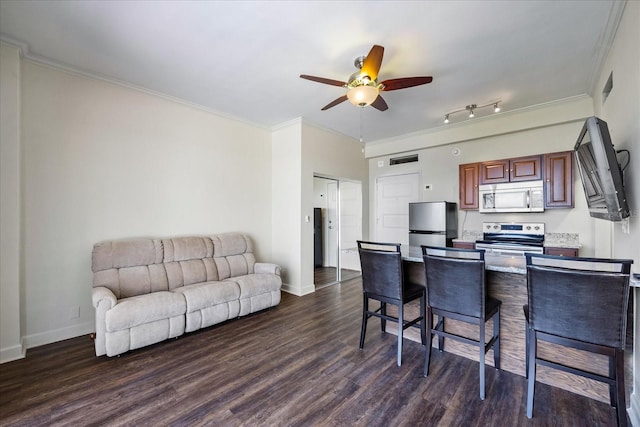 interior space with ceiling fan, dark hardwood / wood-style flooring, a breakfast bar, appliances with stainless steel finishes, and rail lighting