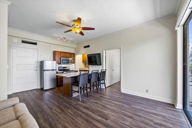 kitchen featuring stainless steel appliances, a kitchen bar, crown molding, dark wood-type flooring, and ceiling fan