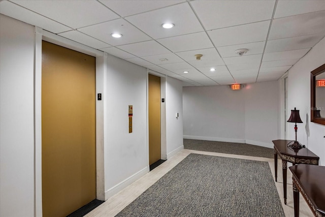 interior space with a paneled ceiling, elevator, and light hardwood / wood-style flooring