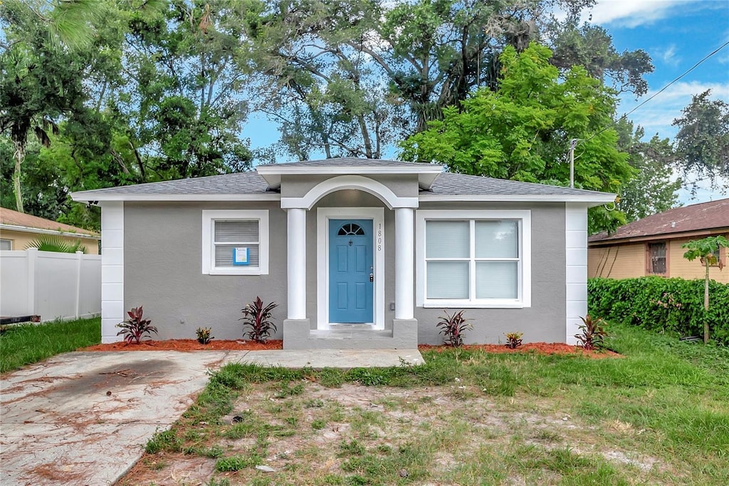 bungalow featuring stucco siding, roof with shingles, a front lawn, and fence