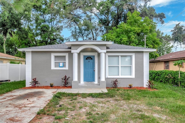 bungalow featuring stucco siding, roof with shingles, a front lawn, and fence