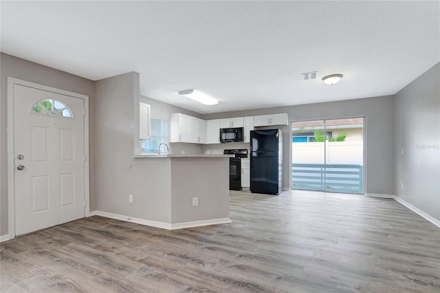 kitchen with kitchen peninsula, white cabinetry, black appliances, and light wood-type flooring