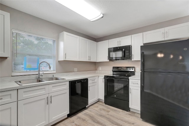 kitchen with white cabinets, black appliances, light hardwood / wood-style floors, and sink