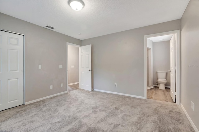 unfurnished bedroom with light colored carpet, a closet, connected bathroom, and a textured ceiling