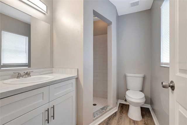 bathroom featuring vanity, a tile shower, hardwood / wood-style floors, and toilet