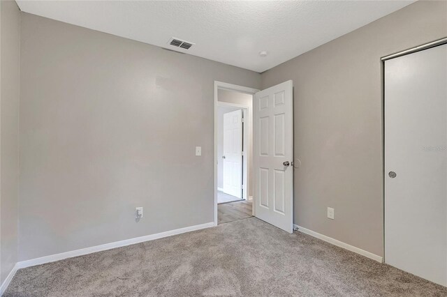 unfurnished bedroom with a textured ceiling, a closet, and light colored carpet