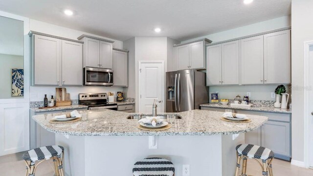 kitchen featuring a kitchen bar, light stone counters, sink, and appliances with stainless steel finishes