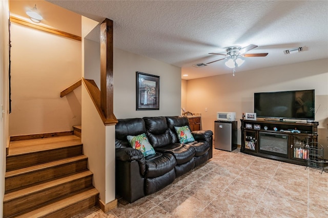 living room with a textured ceiling, stairway, visible vents, and a ceiling fan