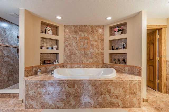 bathroom featuring a textured ceiling, built in shelves, and a bath