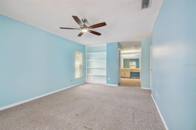 spare room with a textured ceiling, ceiling fan, light carpet, and built in shelves