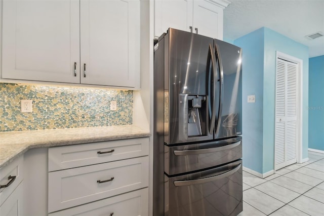 kitchen with stainless steel fridge, backsplash, light tile patterned floors, light stone counters, and white cabinets