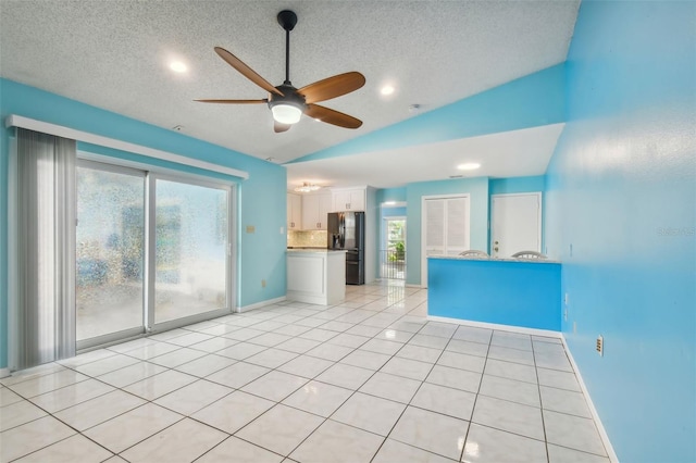 unfurnished living room featuring lofted ceiling, ceiling fan, light tile patterned floors, and a textured ceiling