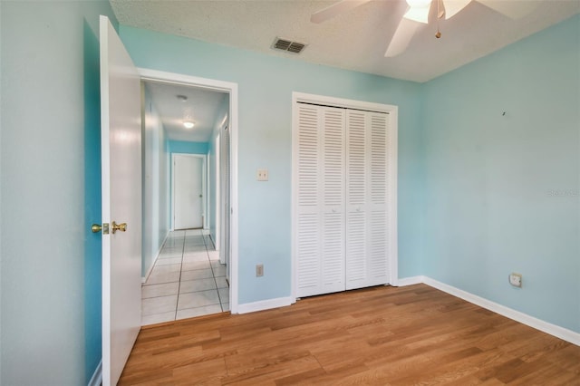 unfurnished bedroom featuring light wood-type flooring, a closet, ceiling fan, and a textured ceiling