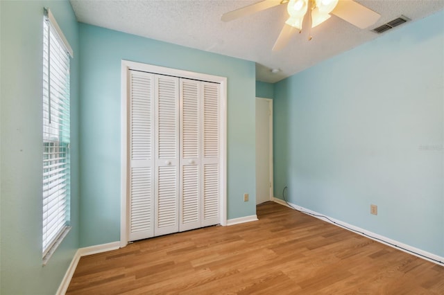 unfurnished bedroom featuring a textured ceiling, ceiling fan, a closet, and light wood-type flooring