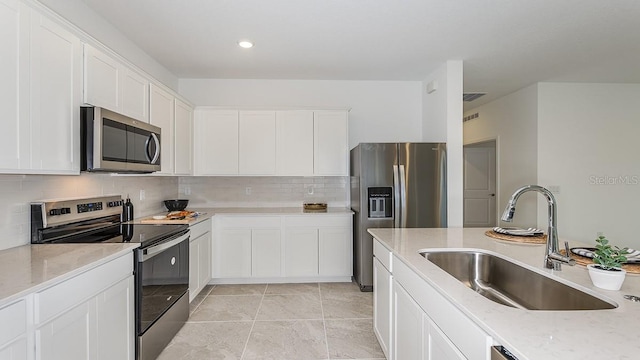 kitchen featuring sink, light tile patterned floors, appliances with stainless steel finishes, light stone countertops, and white cabinets