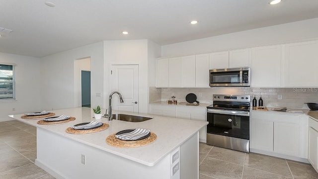 kitchen with sink, light stone counters, stainless steel appliances, a kitchen island with sink, and white cabinets