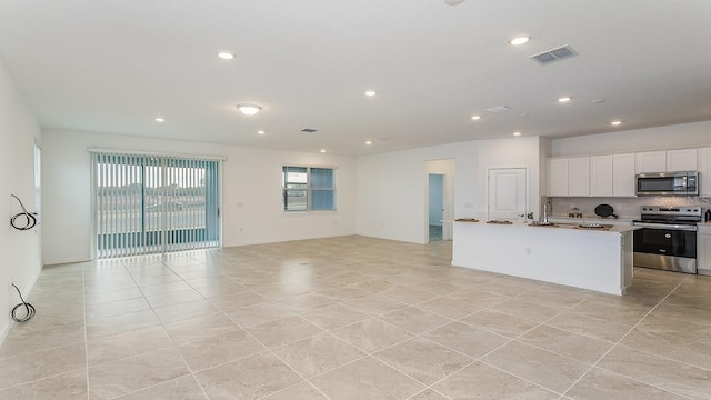 kitchen featuring light tile patterned flooring, white cabinetry, appliances with stainless steel finishes, a kitchen island with sink, and backsplash