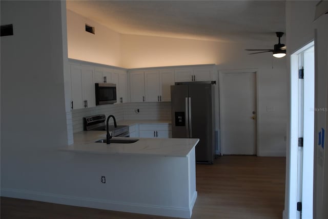 kitchen featuring stainless steel appliances, a peninsula, tasteful backsplash, a ceiling fan, and light wood-type flooring