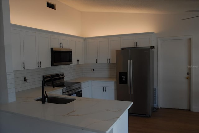 kitchen featuring appliances with stainless steel finishes, a sink, a peninsula, decorative backsplash, and light stone countertops