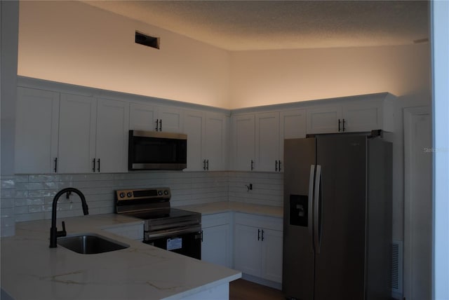kitchen with stainless steel appliances, a sink, light stone countertops, backsplash, and lofted ceiling