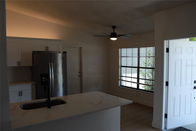kitchen with stainless steel fridge, a ceiling fan, vaulted ceiling, light wood-style flooring, and light stone countertops