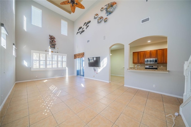 unfurnished living room with light tile patterned floors, sink, ceiling fan, and a high ceiling