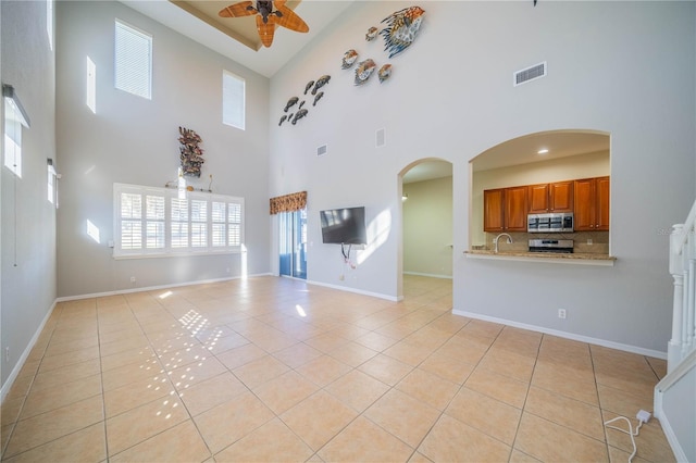 unfurnished living room with light tile patterned floors, baseboards, visible vents, arched walkways, and a ceiling fan