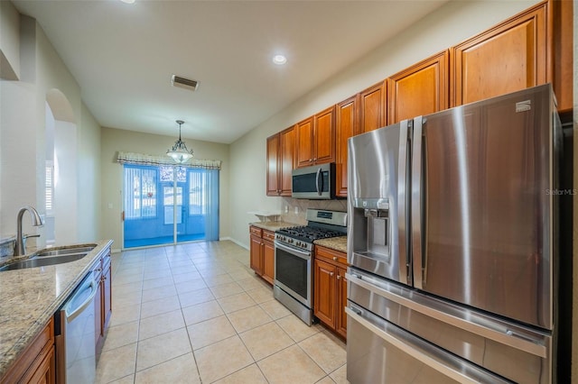 kitchen featuring visible vents, appliances with stainless steel finishes, brown cabinetry, a sink, and light stone countertops