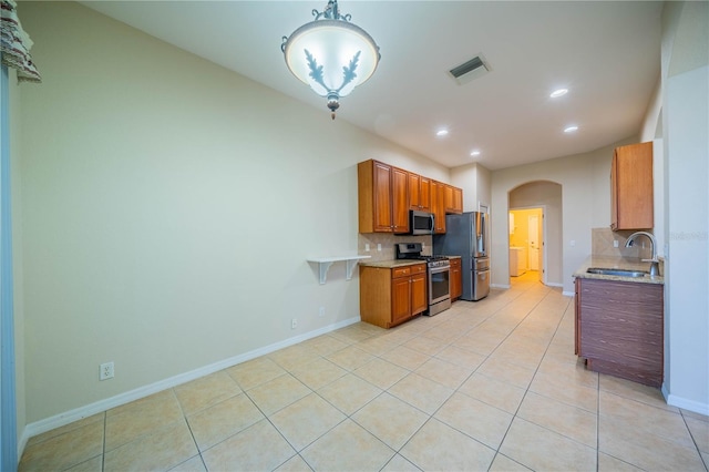 kitchen featuring arched walkways, stainless steel appliances, a sink, visible vents, and tasteful backsplash