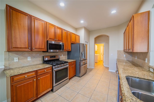 kitchen featuring light tile patterned floors, arched walkways, brown cabinetry, appliances with stainless steel finishes, and a sink