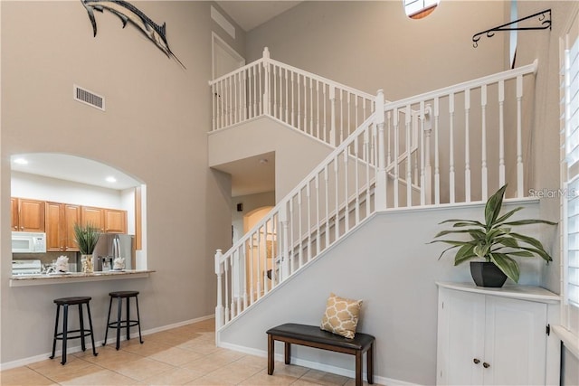 staircase featuring arched walkways, visible vents, a high ceiling, and tile patterned floors