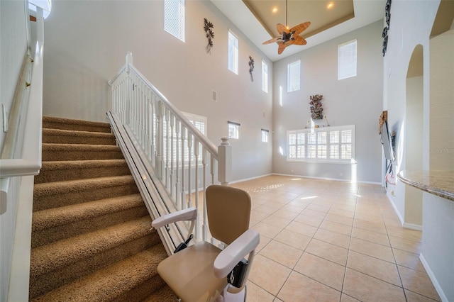 stairway with a towering ceiling, a tray ceiling, tile patterned floors, and ceiling fan