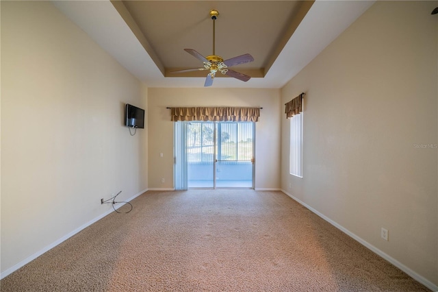 carpeted spare room with ceiling fan, a tray ceiling, and baseboards