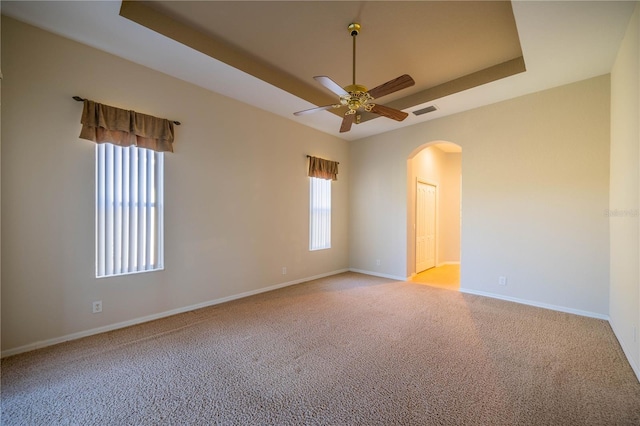carpeted spare room featuring baseboards, visible vents, a raised ceiling, and arched walkways
