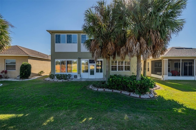 rear view of house featuring a sunroom, a lawn, and stucco siding