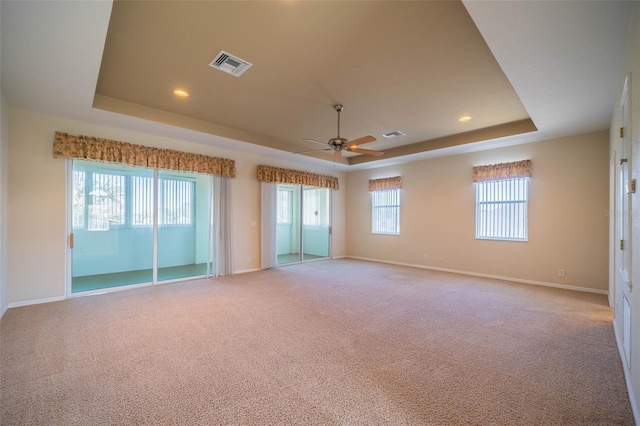 unfurnished room featuring a tray ceiling, ceiling fan, and light colored carpet