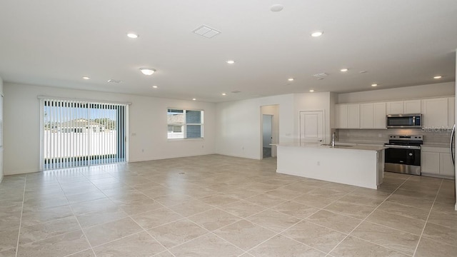 kitchen featuring sink, white cabinetry, stainless steel appliances, tasteful backsplash, and a center island with sink