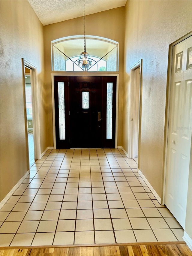 entryway with an inviting chandelier, light hardwood / wood-style floors, high vaulted ceiling, and a textured ceiling