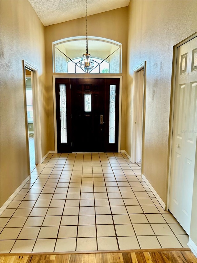 foyer featuring light tile patterned floors, baseboards, high vaulted ceiling, and a textured ceiling