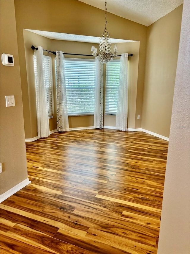 unfurnished dining area with a notable chandelier, baseboards, vaulted ceiling, and wood finished floors