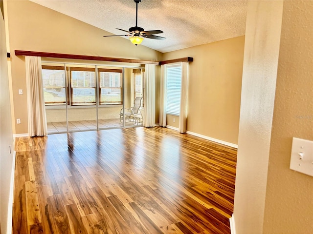 empty room featuring ceiling fan, vaulted ceiling, a textured ceiling, and wood finished floors