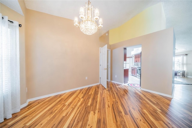 empty room featuring ceiling fan with notable chandelier, lofted ceiling, and hardwood / wood-style flooring