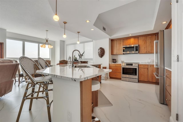 kitchen featuring brown cabinetry, a breakfast bar, stainless steel appliances, pendant lighting, and a sink