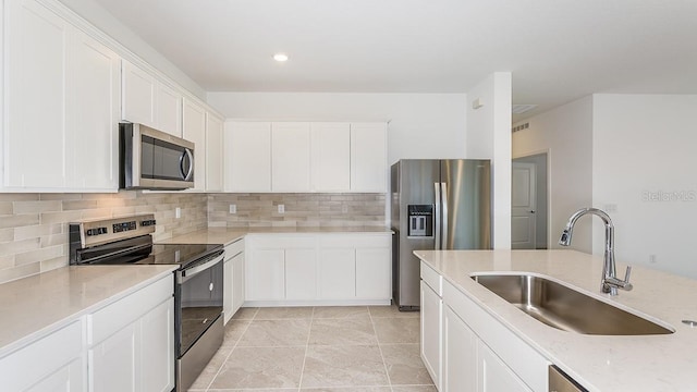 kitchen with sink, stainless steel appliances, tasteful backsplash, light stone countertops, and white cabinets