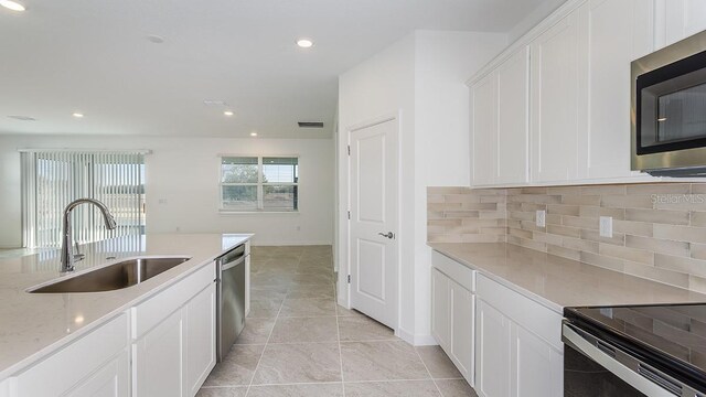 kitchen with appliances with stainless steel finishes, sink, white cabinets, backsplash, and light tile patterned floors